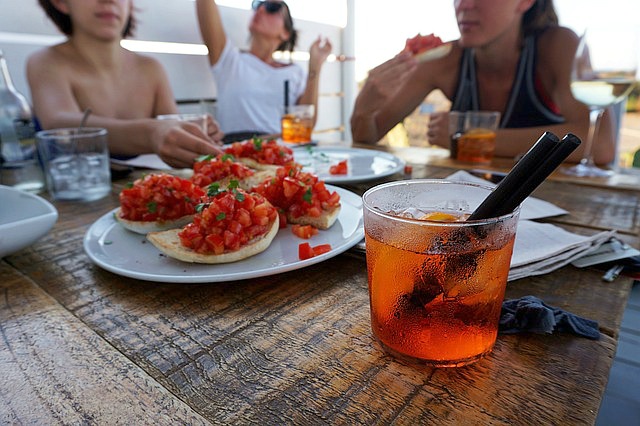 people drinking spritz cocktail and eating tomato bruschetta bread